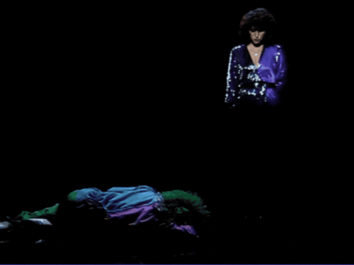 a woman with curly hair singing into a microphone in a dark room