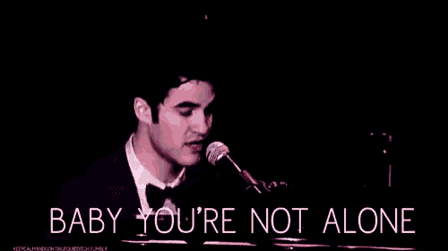 a man in a tuxedo is singing into a microphone while playing the piano .