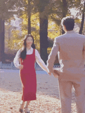 a woman in a red dress is holding a man 's hand in a park