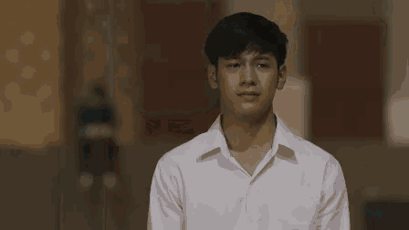 a young man in a white shirt is standing in front of a wall and crying .
