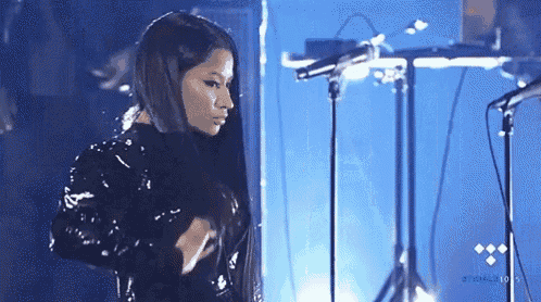 a woman is standing in front of a microphone on a stage and adjusting her hair .