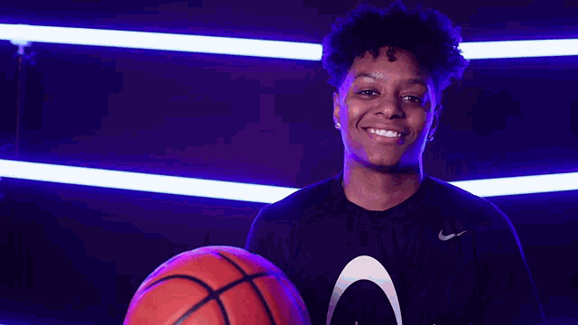 a young man in a nike shirt is holding a basketball and smiling