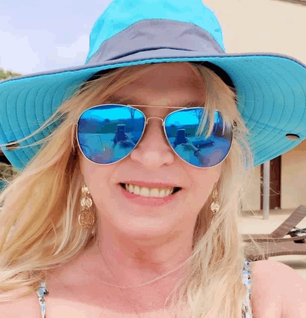 a woman wearing a blue hat and blue sunglasses smiles for the camera