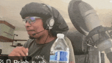 a man wearing headphones holds a bottle of kirkland water in front of a microphone