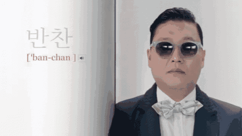 a man wearing sunglasses and a bow tie stands in front of a book that says ' ban-chan '