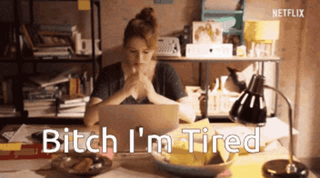 a woman is sitting at a desk with a laptop and the words bitch i 'm tired