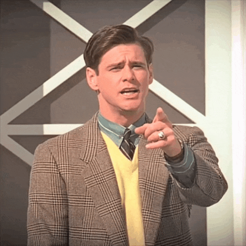a man wearing a plaid jacket and a yellow sweater is pointing at the camera