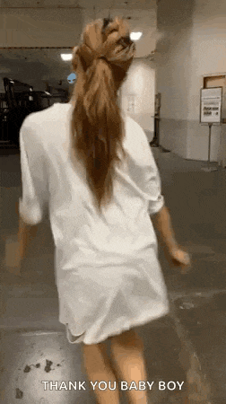a woman is wearing a white shirt and a ponytail while walking down a hallway .