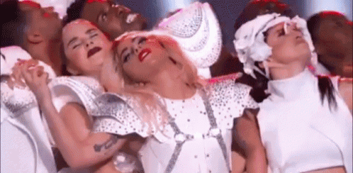 a group of dancers are standing around a woman in a white dress .