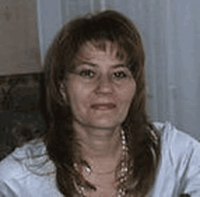 a woman wearing a white shirt and a necklace is sitting in a chair and looking at the camera .