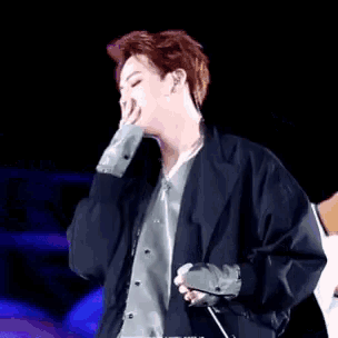 a man in a black jacket is singing into a microphone while dancing on a stage .