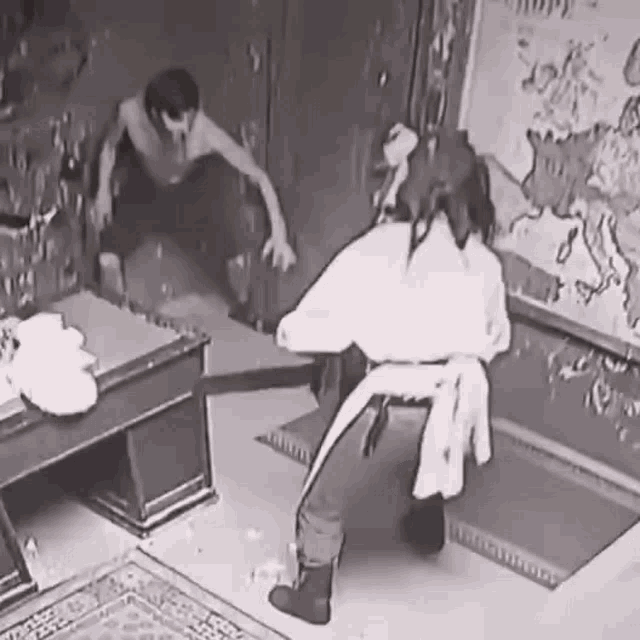 a black and white photo of a man sitting on a chair and a woman sitting at a table .