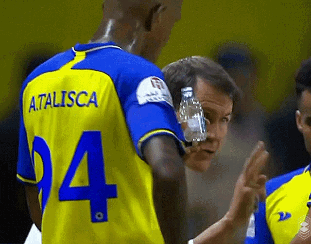 a man wearing a yellow and blue a.talisca jersey holds a bottle of water to his face