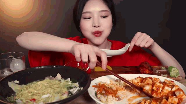 a woman in a red shirt is eating a bowl of noodles with chopsticks