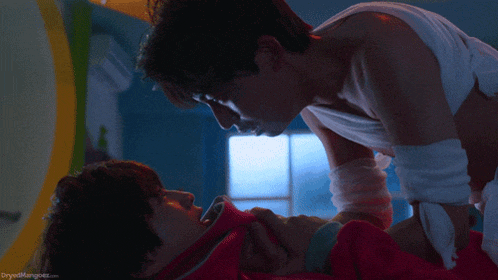 two men are kissing in a room with the words dryedmangoes.com on the bottom left