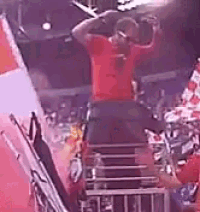 a man in a red shirt is standing on a stage with his arms up in the air .