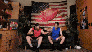 two men sitting on a couch in front of an american flag with a football on it