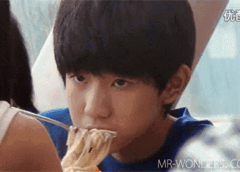 a young boy is eating noodles with a fork while sitting at a table .