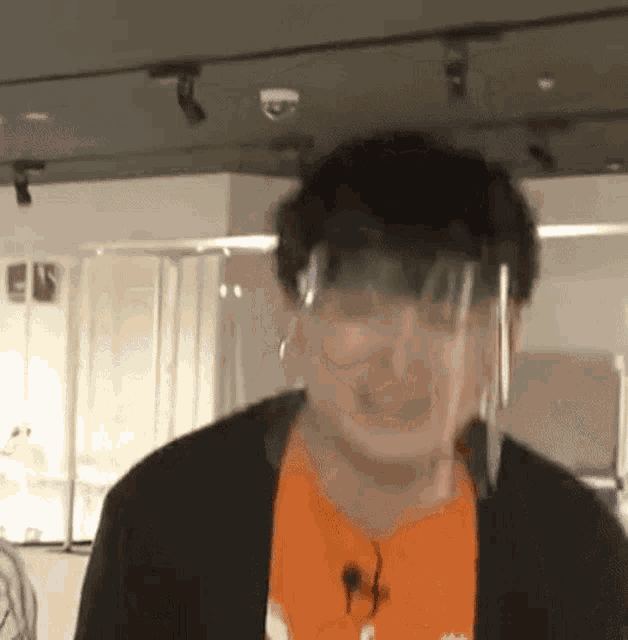 a man wearing a face shield and an orange shirt is standing in a room .