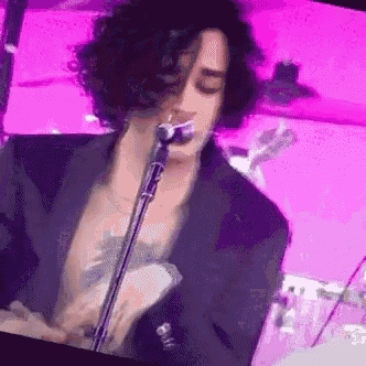 a woman with curly hair is singing into a microphone while playing drums .