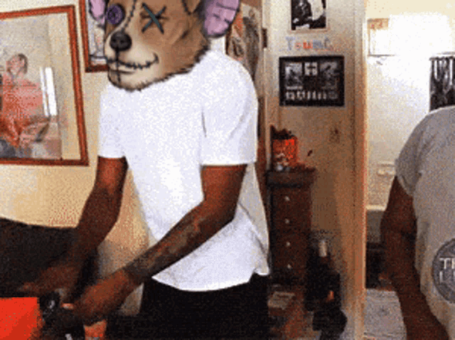 a man wearing a teddy bear mask is standing in front of a wall that says t-u-nc