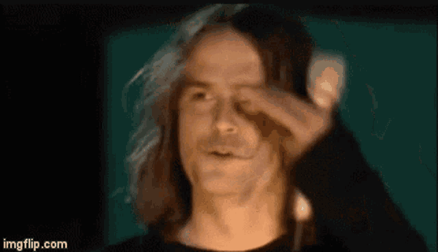 a man with long hair is holding his hand to his face and making a funny face .