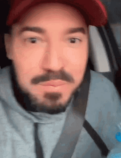 a man with a beard is wearing a red hat and a seat belt .