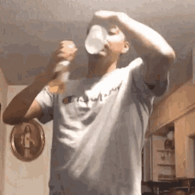 a man in a champion shirt is drinking from a bottle in a kitchen .
