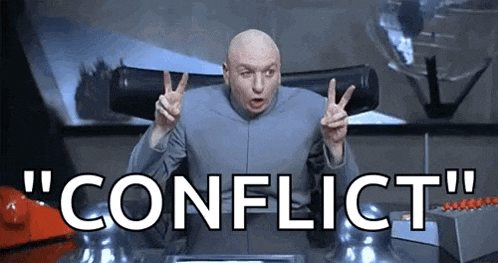 a bald man is giving a peace sign while sitting at a desk with the word conflict .