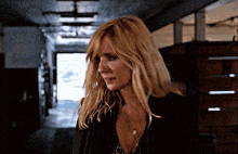 a woman with blonde hair is standing in a hallway looking at the camera
