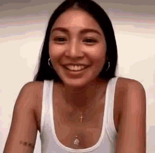 the woman is wearing a white tank top and a cross necklace .