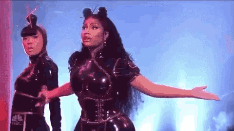 a woman is dancing on a stage with her arms outstretched while another woman looks on .