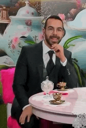 a man in a suit and tie is sitting at a table with a cup of coffee .