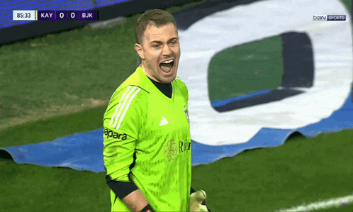 a soccer player wearing a green adidas jersey screams during a game