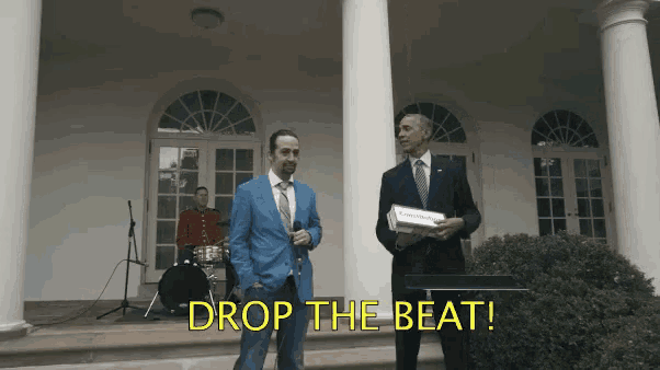 a man in a blue suit stands next to a man in a suit holding a box that says drop the beat on it