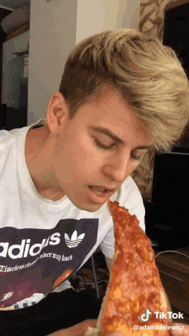 a man wearing an adidas shirt is eating a large slice of pizza