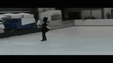 a woman in a black dress is ice skating on an indoor ice rink