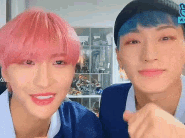 two young men with pink hair and blue hair are sitting next to each other and smiling .