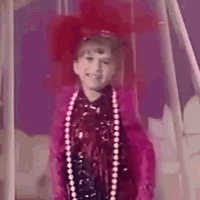 a little girl is wearing a pink jacket and a red hat and smiling .