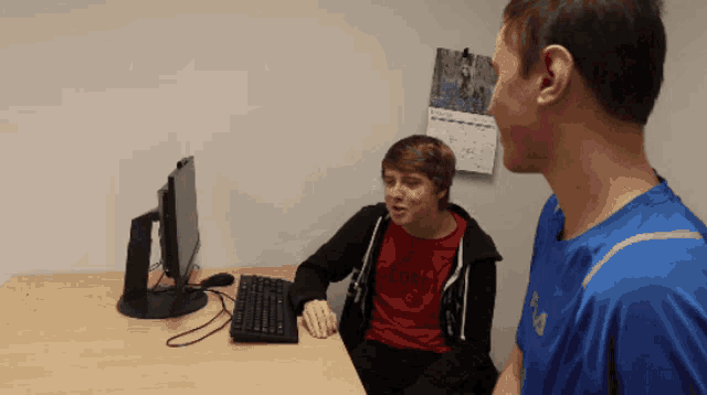 a boy wearing a red shirt that says genesis is sitting at a desk