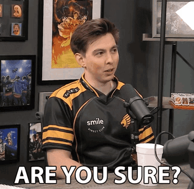 a man wearing a smile direct club shirt is sitting in front of a microphone and asking are you sure