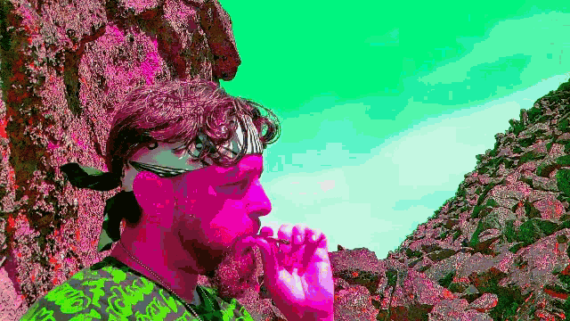 a man with a bandana on his head is smoking a cigarette in front of a rocky cliff