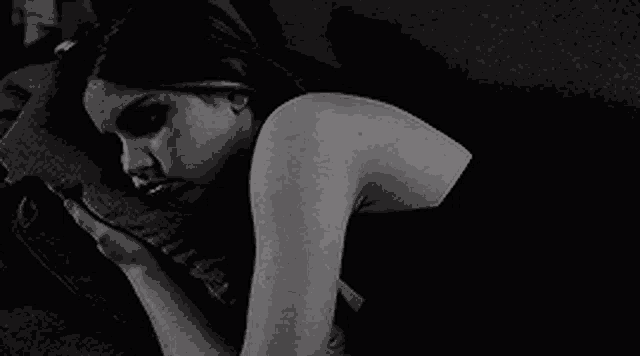 a black and white photo of a woman laying on a couch holding a pillow .