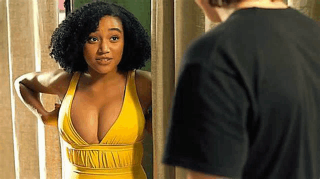 a woman in a yellow swimsuit is standing next to a man in a black shirt and looking at herself in the mirror .