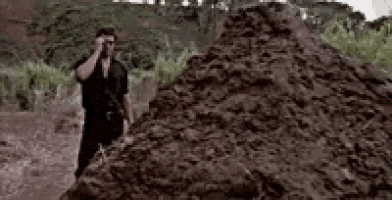 a man is standing next to a pile of dirt in a field .