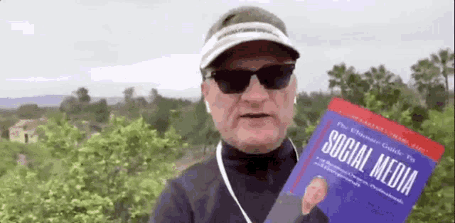 a man wearing sunglasses and a hat is holding a book about social media