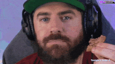 a man with a beard wearing headphones and a hat eating a cookie