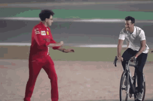 a man in a red jumpsuit is standing next to a man riding a bicycle .
