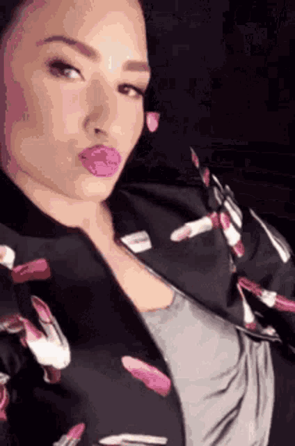 a woman wearing a jacket with lipsticks on it is taking a selfie .