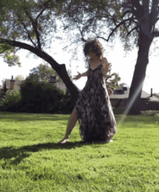 a woman in a long dress is standing in the grass with her arms outstretched